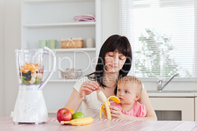 Attractive brunette woman pealing a banana while holding her bab