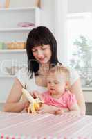 Beautiful brunette woman pealing a banana while holding her baby