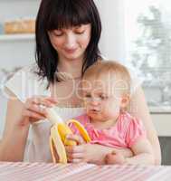 Charming brunette woman pealing a banana while holding her baby