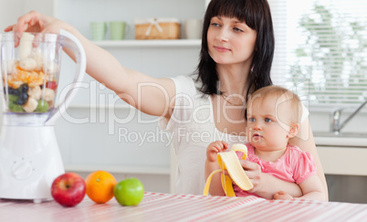 Gorgeous brunette woman putting vegetables in a mixer while hold