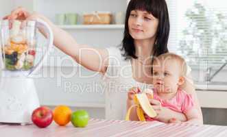 Gorgeous brunette woman putting vegetables in a mixer while hold