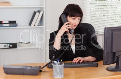 Attractive brunette woman on the phone while working on a comput