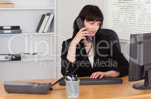Attractive brunette woman on the phone while working on a comput