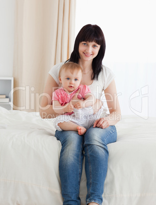 Beautiful brunette woman holding her baby on her knees while sit