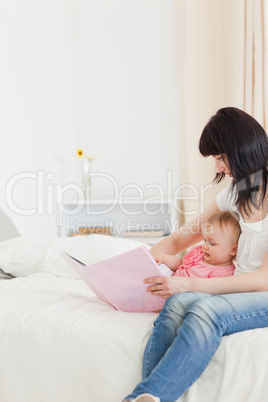 Good looking brunette woman showing a book to her baby while sit