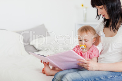 Pretty brunette woman showing a book to her baby while sitting o