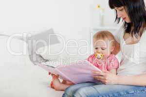 Pretty brunette woman showing a book to her baby while sitting o