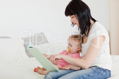 Lovely brunette woman showing a book to her baby while sitting o