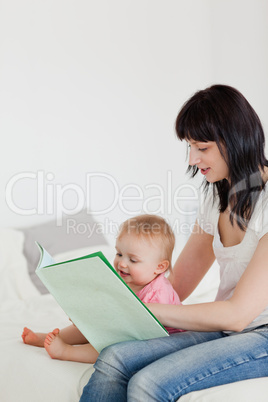Cute brunette woman showing a book to her baby while sitting on