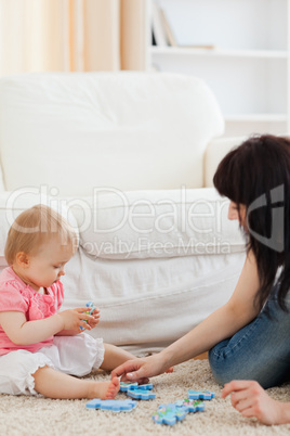 Attractive woman and her baby playing with puzzle pieces while s