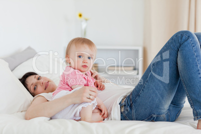 Charming brunette woman posing with her baby while lying on a be