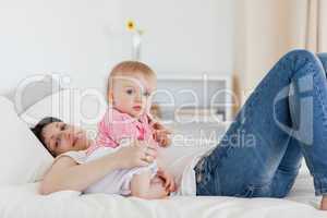 Charming brunette woman posing with her baby while lying on a be