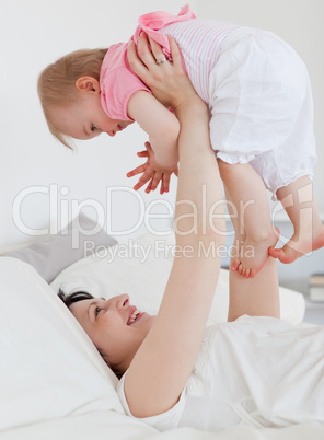 Gorgeous brunette woman playing with her baby while lying on a b