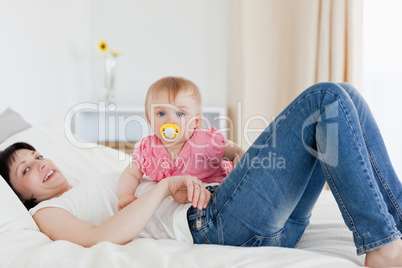 Beautiful brunette woman posing with her baby while lying on a b