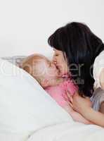 Lovely brunette woman giving a kiss to her baby on a bed