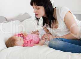 Pretty brunette female playing with her baby while lying on a be