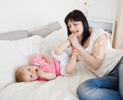 Attractive brunette female playing with her baby while lying on