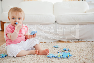 Cute baby playing with puzzle pieces while sitting on a carpet