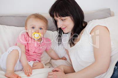 Attractive brunette female looking at her baby while lying on a