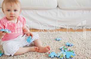 Lovely baby playing with puzzle pieces while sitting on a carpet