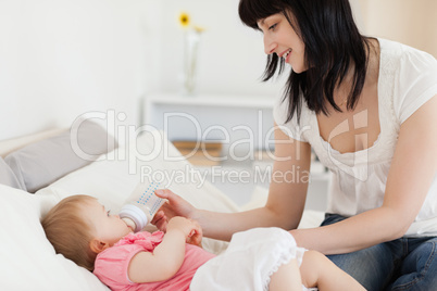 Attractive brunette female bottle-feeding her baby on a bed