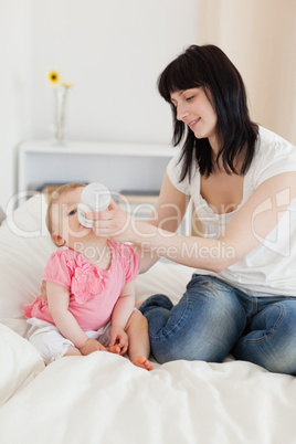 Pretty brunette female bottle-feeding her baby on a bed