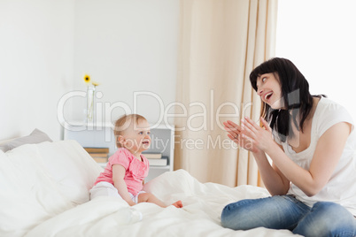 Gorgeous brunette female playing with her baby while sitting on