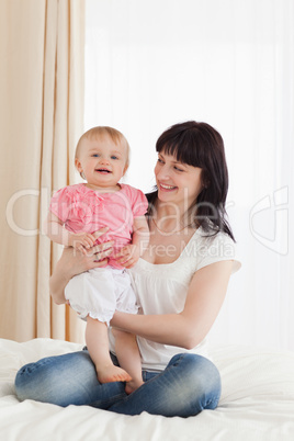 Cute brunette woman holding her baby on her knees while sitting