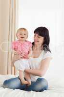 Cute brunette woman holding her baby on her knees while sitting