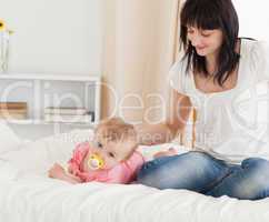Cute brunette woman looking at her lying baby on a bed