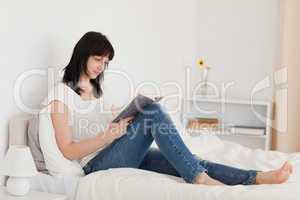 Beautiful brunette woman reading a book while sitting on a bed
