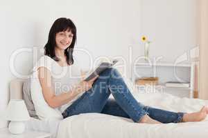Attractive brunette woman reading a book while sitting on a bed