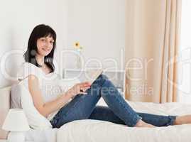 Gorgeous brunette woman reading a book while sitting on a bed