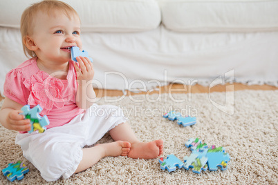 Blond baby playing with puzzle pieces while sitting on a carpet