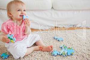 Blond baby playing with puzzle pieces while sitting on a carpet