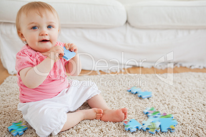 Cute blond baby playing with puzzle pieces while sitting on a ca