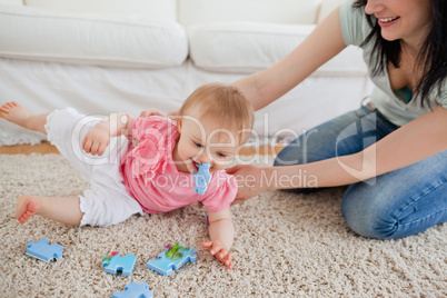 Lovely woman and her baby playing with puzzle pieces while sitti