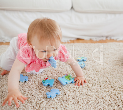 Lovely blond baby playing with puzzle pieces on a carpet