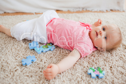 Cute blond baby playing with puzzle pieces while lying on a carp