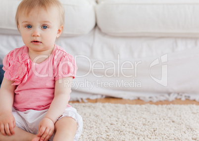 Lovely blond baby looking at the camera while sitting on a carpe