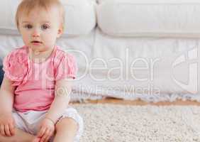 Lovely blond baby looking at the camera while sitting on a carpe