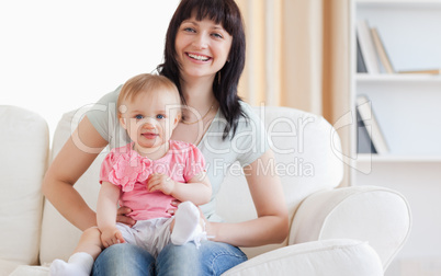 Pretty woman holding her baby in her arms while sitting on a sof