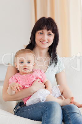 Charming woman holding her baby in her arms while sitting on a s