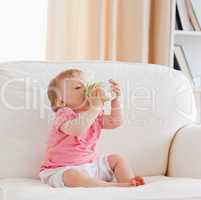 Lovely blond baby bottle-feeding while sitting on a sofa