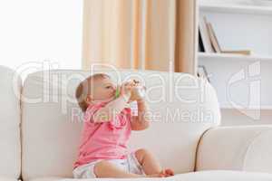 Cute blond baby bottle-feeding while sitting on a sofa
