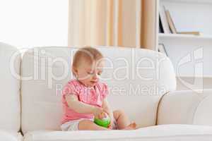 Cute blond baby playing with a ball while sitting on a sofa