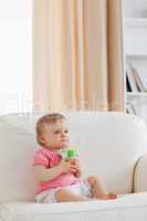 Lovely blond baby playing with a ball while sitting on a sofa
