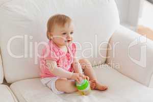 Blond baby playing with a ball while sitting on a sofa