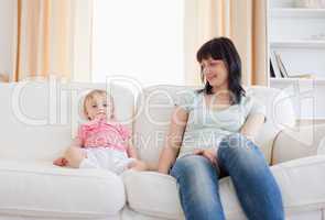 Pretty woman looking at her baby while sitting on a sofa