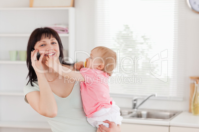 Lovely woman on the phone while holding her baby in her arms